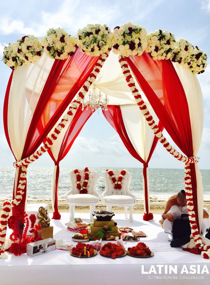 a man and woman sitting under a red and white canopy on the beach with food