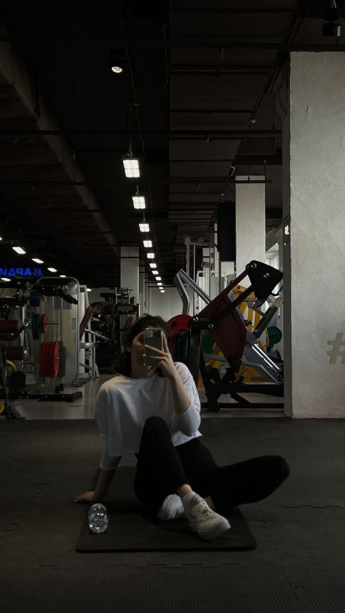 a woman sitting on the ground while talking on her cell phone in a gym area