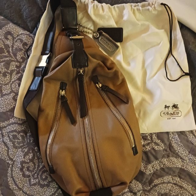 a brown purse sitting on top of a bed next to a cell phone