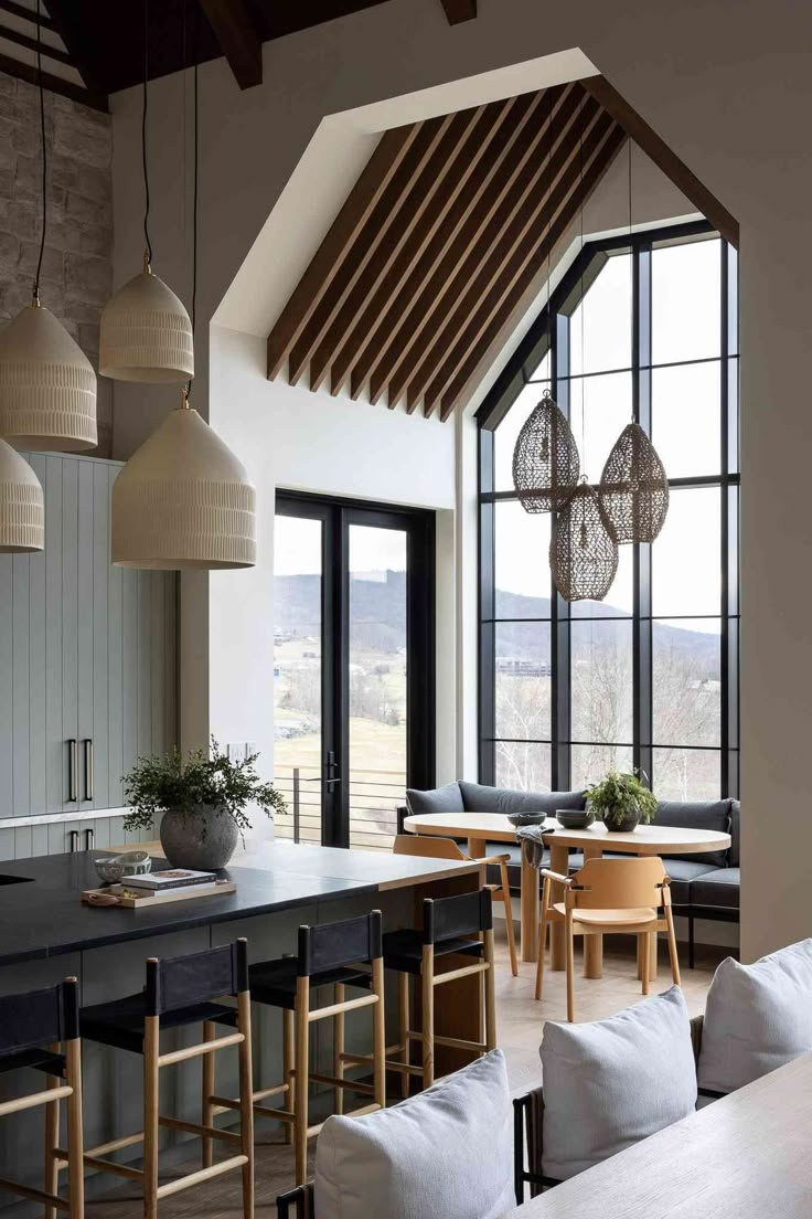 an open kitchen and dining area with large windows, wooden beams and modern lighting fixtures