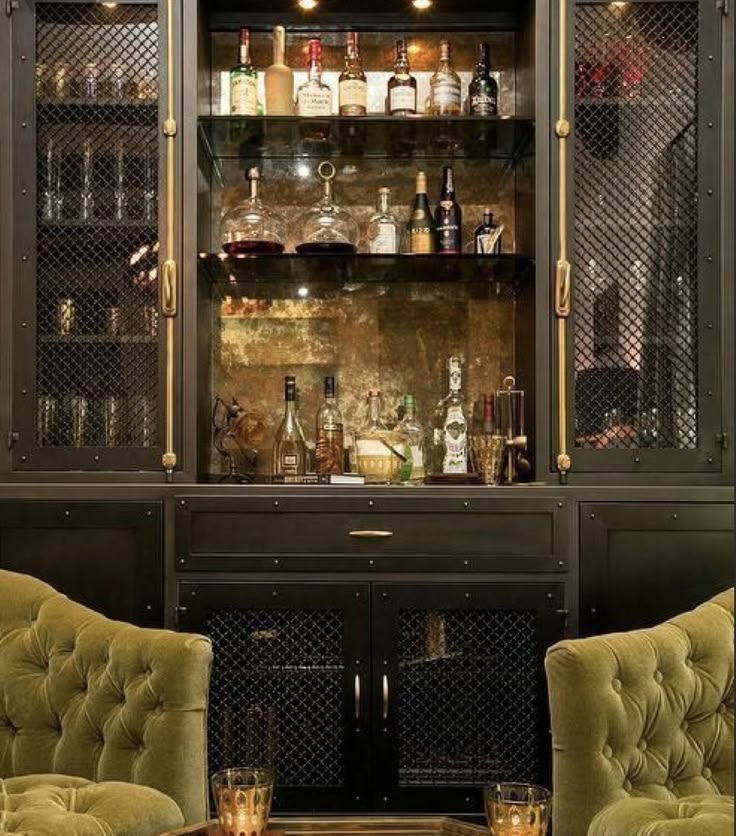 two green velvet chairs sitting in front of a bar with liquor bottles on the shelves