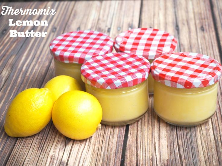 three lemon butter jars sitting on top of a wooden table next to two lemons