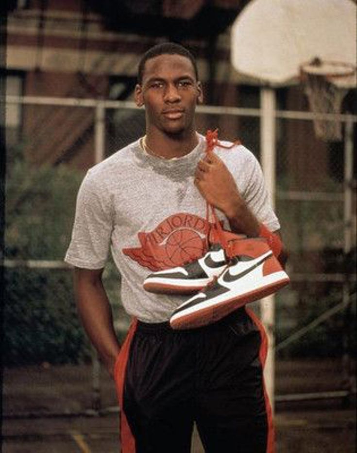 a man holding a pair of shoes in his left hand while standing on a basketball court