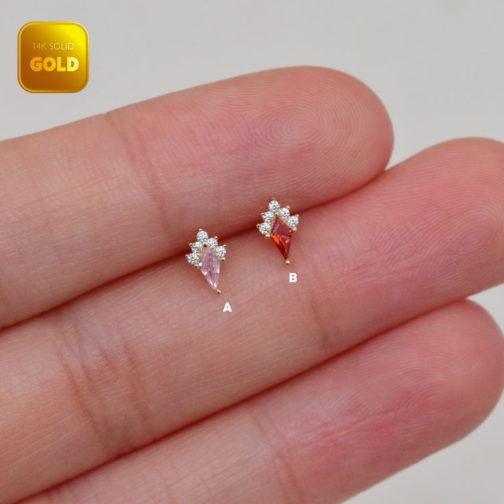 the tiny diamond earrings are being held in someone's hand with gold lettering on it