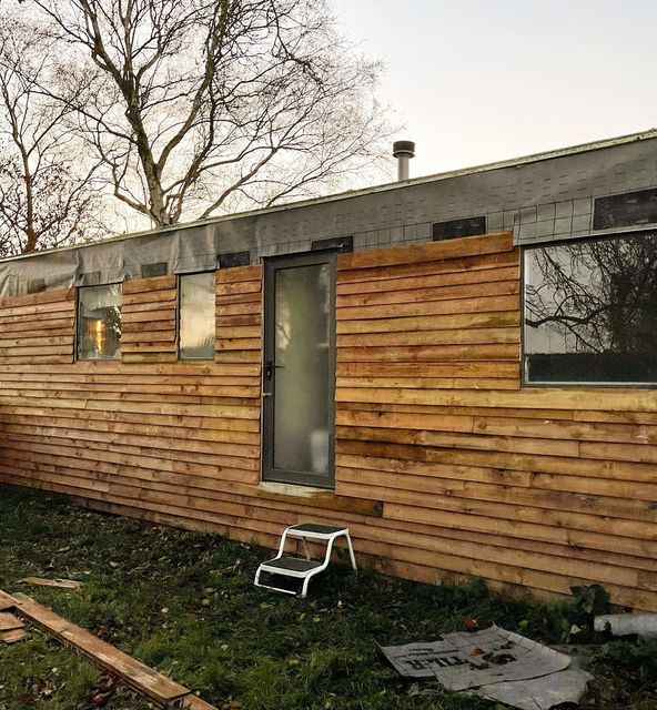 a small wooden house sitting on top of a grass covered field next to a tree