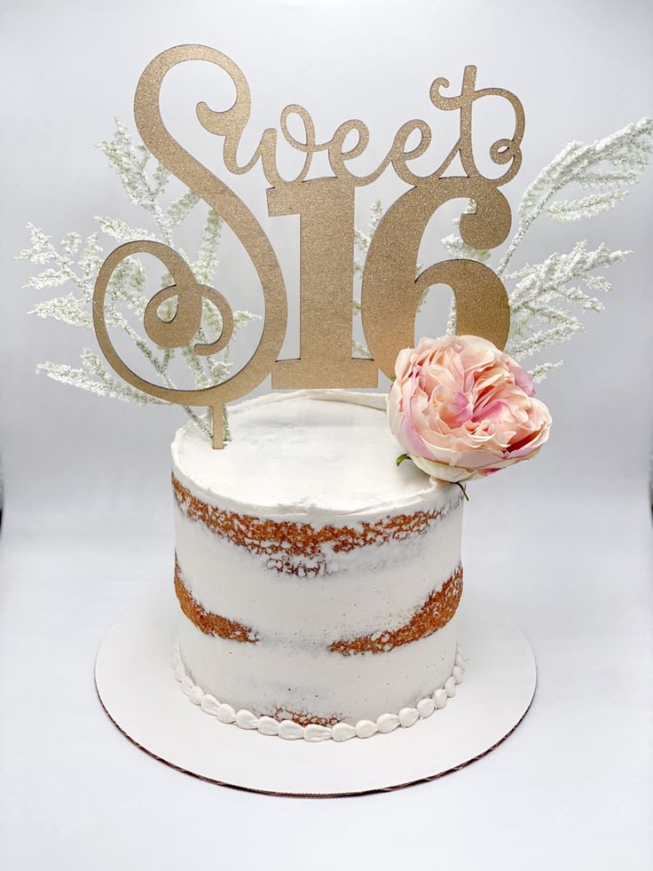 a white cake topped with a frosted number and a pink flower sitting on top of it