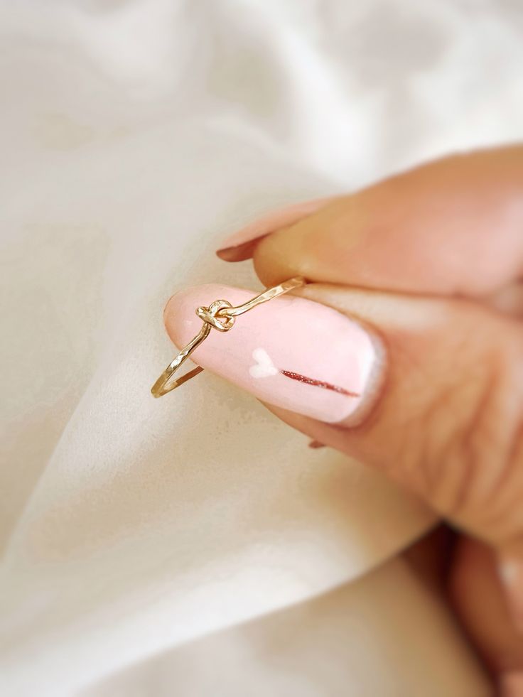 a woman's hand holding a pink ring with a diamond on the middle and a gold band around it