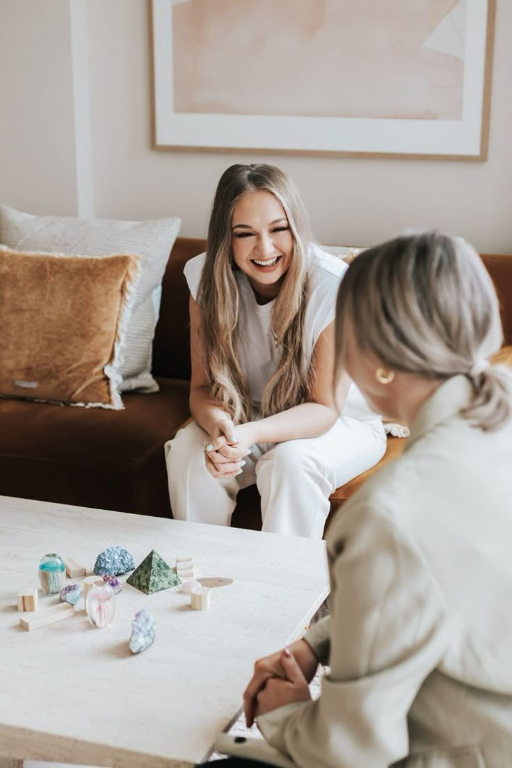 two women sitting at a table and playing with blocks in front of the woman on the couch