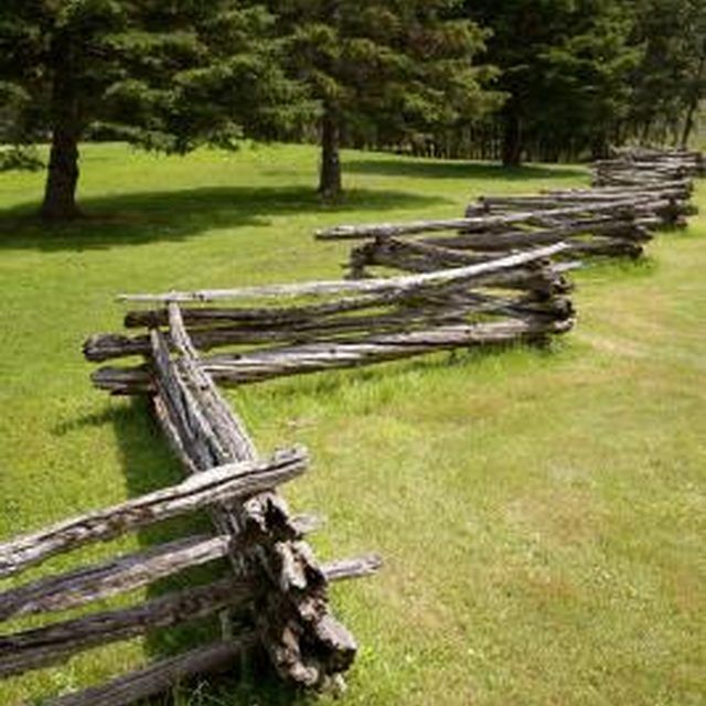 an old wooden fence in the middle of a grassy field with trees and grass behind it