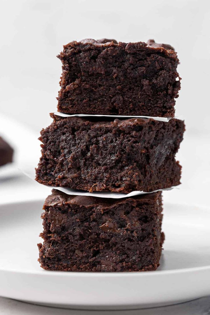 three chocolate brownies stacked on top of each other in front of a white plate