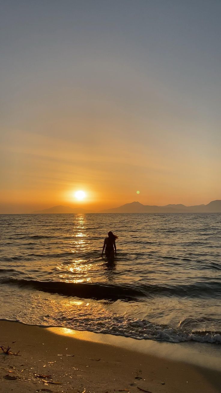 a person wading in the ocean at sunset