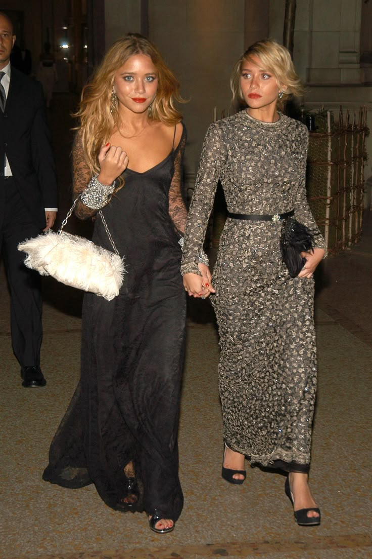 two women walking down the street holding hands and wearing evening dresses with feathers on them