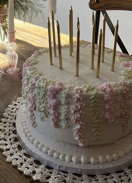 a white cake with pink flowers and gold candles on it sitting on a doily