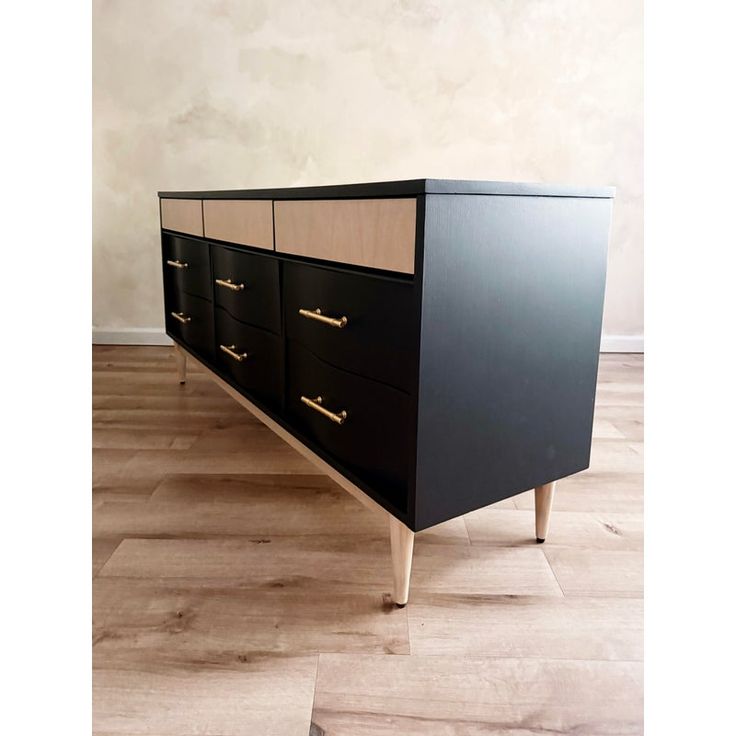 a black and white dresser with gold handles on it's sides in an empty room