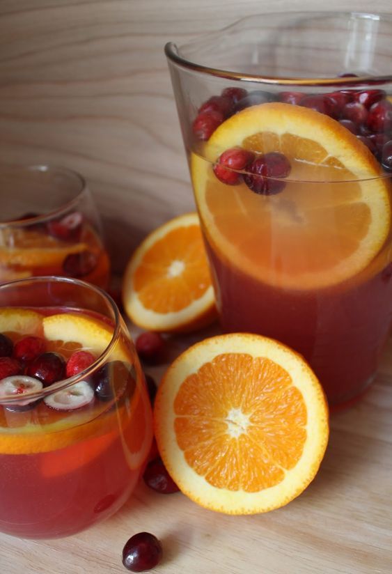 oranges, cranberries and cherries are in glasses on a wooden table