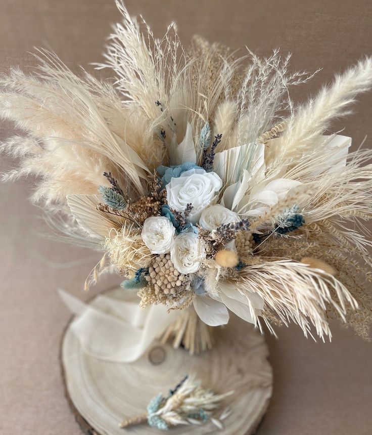 an arrangement of dried flowers and feathers in a vase