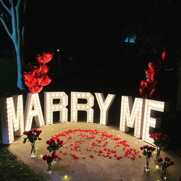 a lighted sign that says marry me surrounded by flowers and candles in the shape of letters