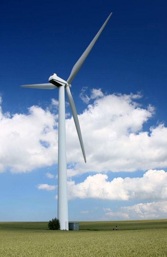 a wind turbine in the middle of a field with blue sky and clouds behind it