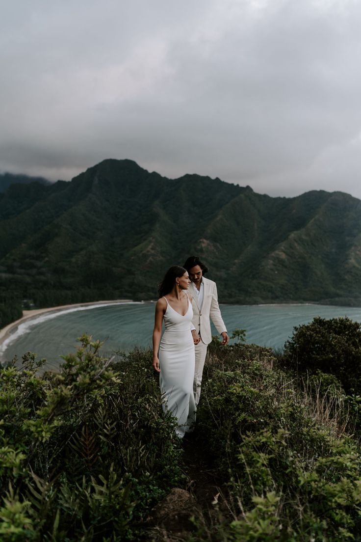 a bride and groom walking down a hill by the ocean