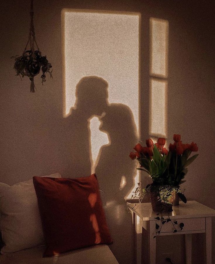 the shadow of a person standing in front of a window next to a table with flowers on it