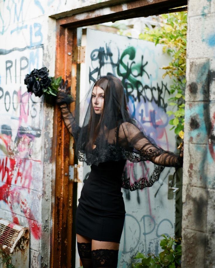 a woman dressed in black posing for a photo with graffiti on the wall behind her