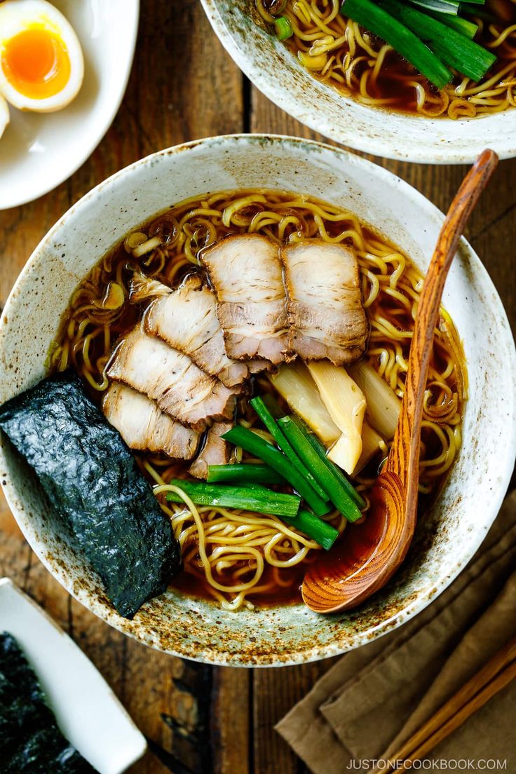 two bowls filled with noodles, meat and veggies on top of a wooden table