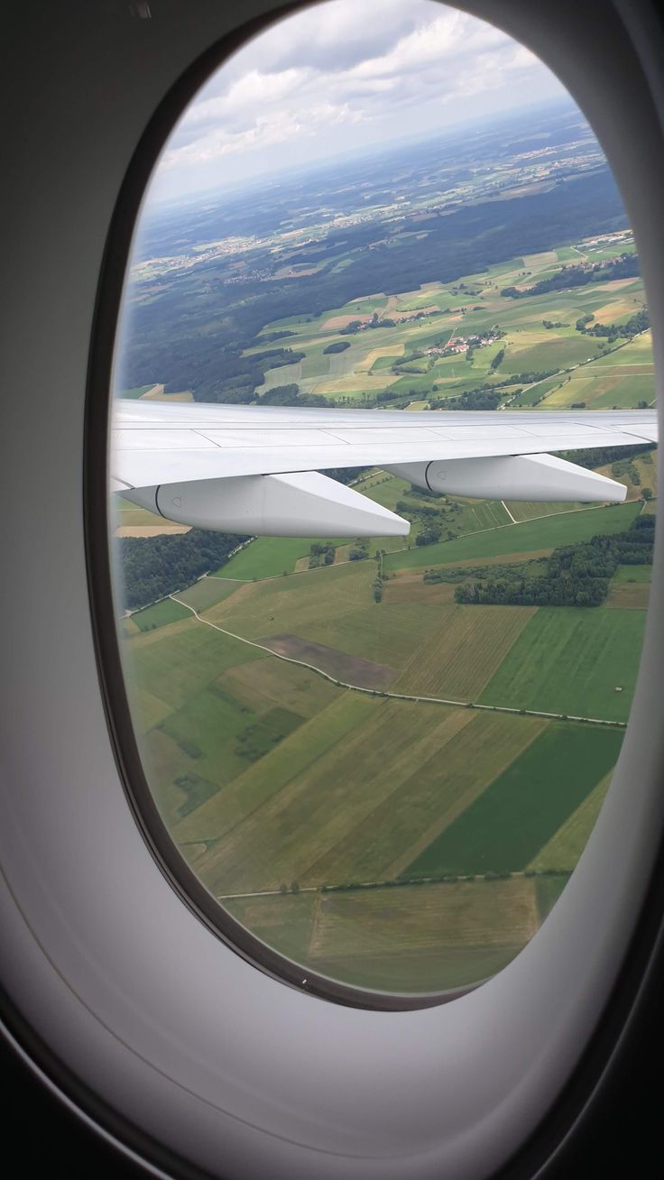 the view from an airplane window looking out over farmlands and fields in the distance