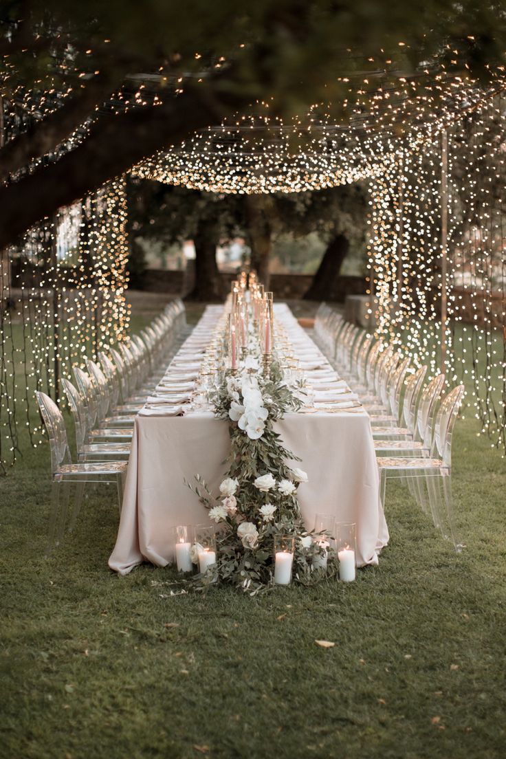 a long table with white flowers and candles on it in the middle of an outdoor setting