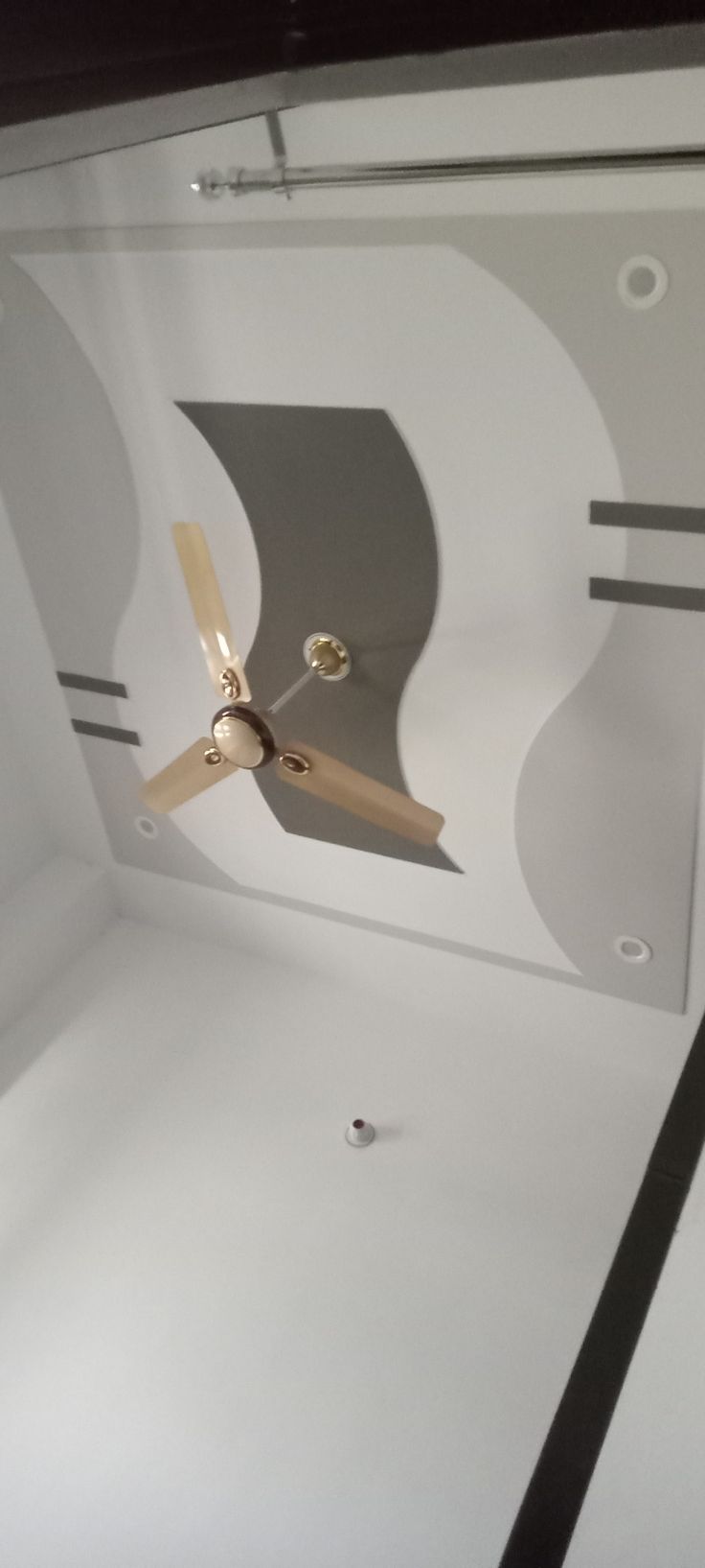 a ceiling fan in the middle of a room with white walls and black flooring