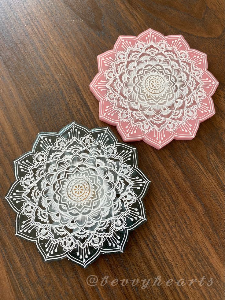 two decorative coasters sitting on top of a wooden table with white and pink designs