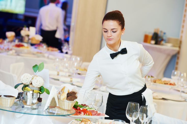 a woman standing in front of a table with food and wine glasses on top of it