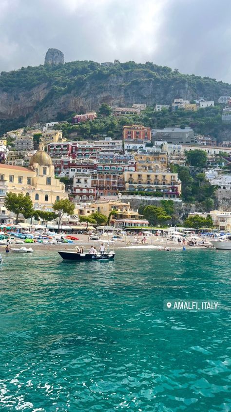 some boats are in the water and buildings on top of a hill behind them is a beach