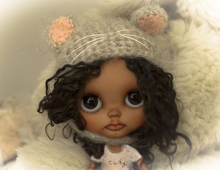 a close up of a doll with big eyes wearing a cat hat and fur coat