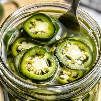 pickled jalapenos in a jar with a spoon on the side, ready to be eaten