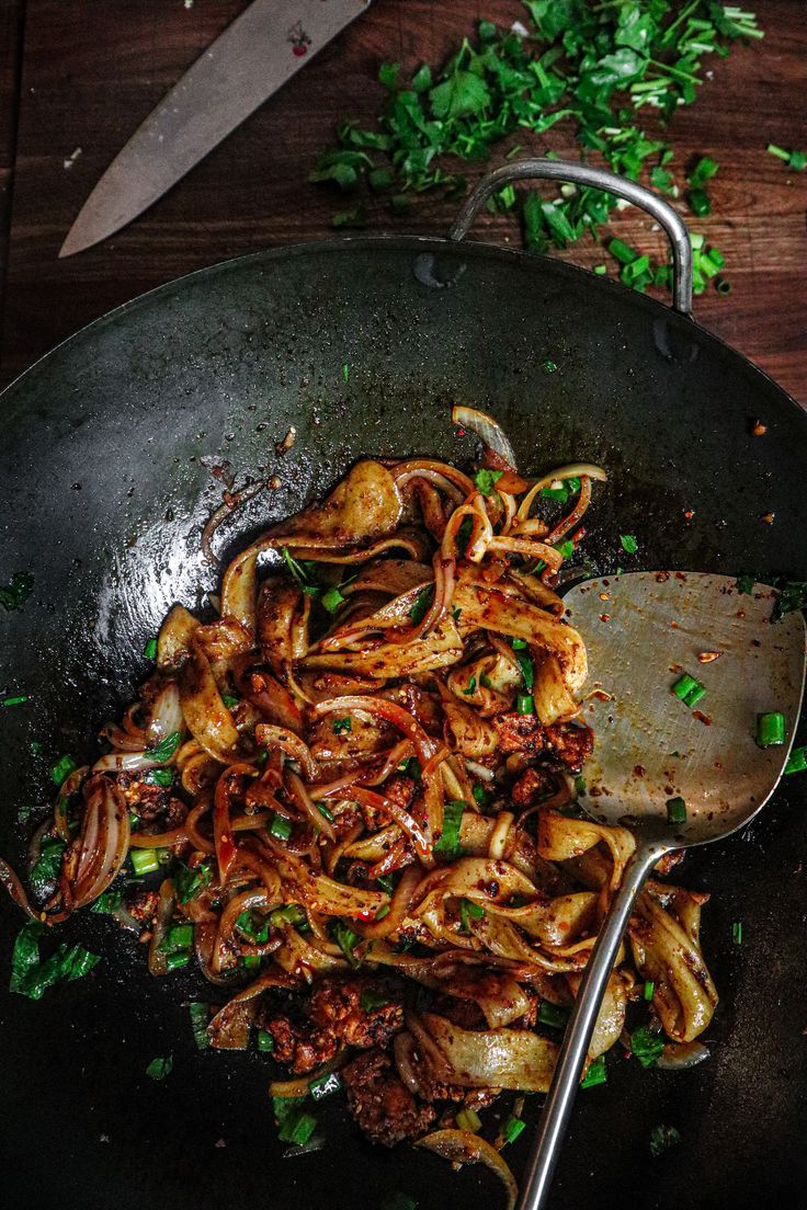 a wok filled with pasta and meat on top of a wooden table