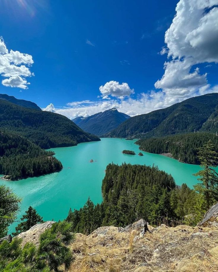 a lake surrounded by mountains and trees under a blue sky with clouds in the background