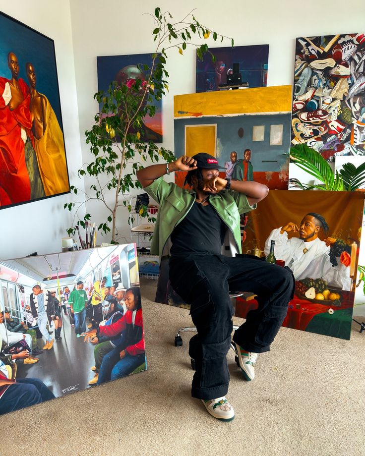 a man standing in front of several paintings on the wall with his hands behind his head