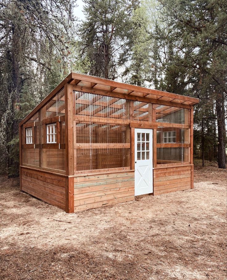 a small wooden building with a white door and windows in the middle of a forest