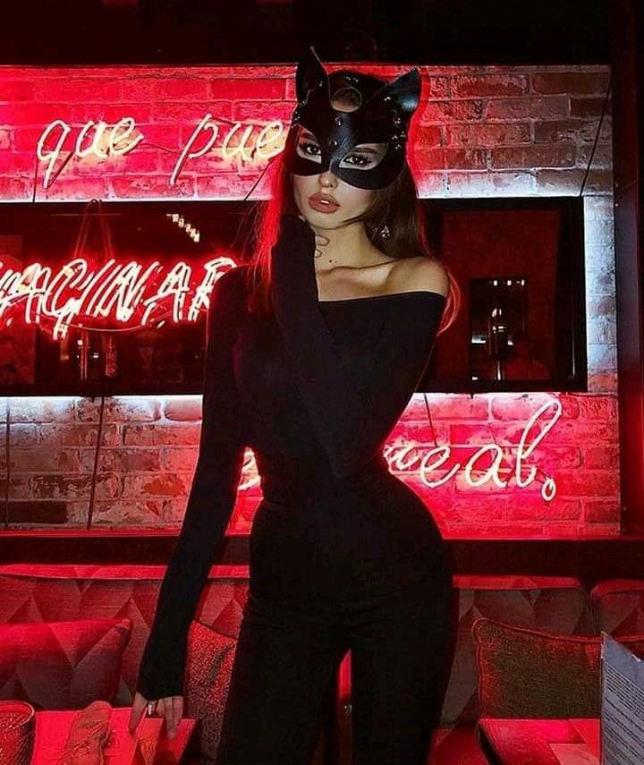 a woman wearing a cat mask standing in front of a neon sign