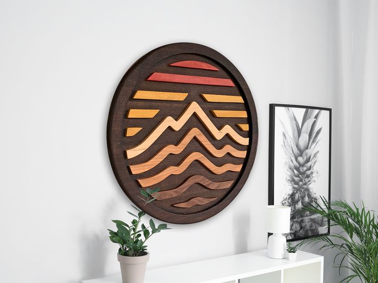 a wooden wall hanging on the side of a white wall next to a potted plant