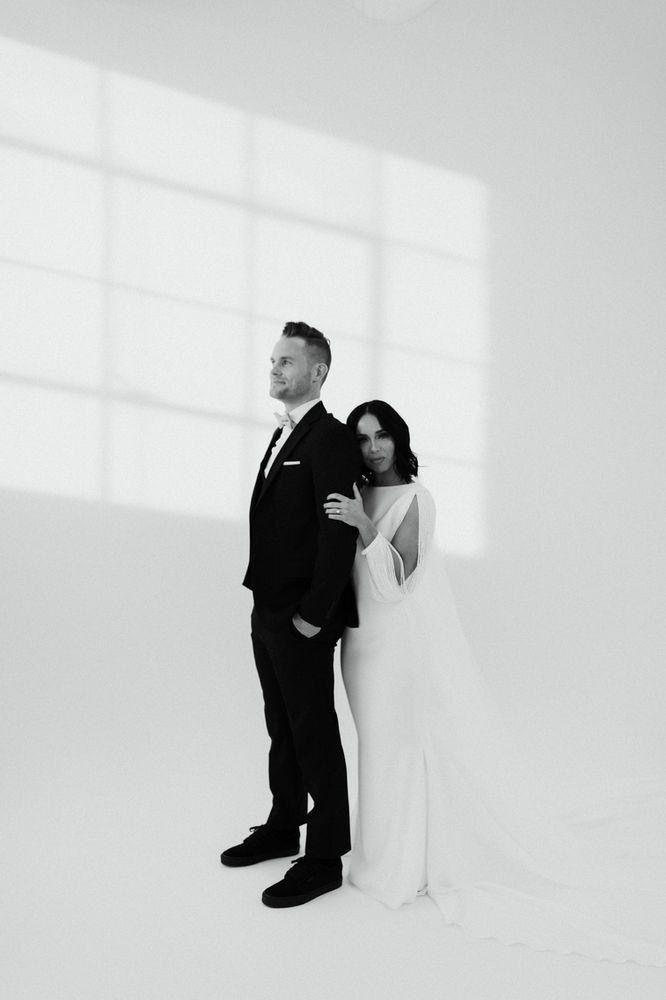 a man and woman standing next to each other in front of a white wall with windows