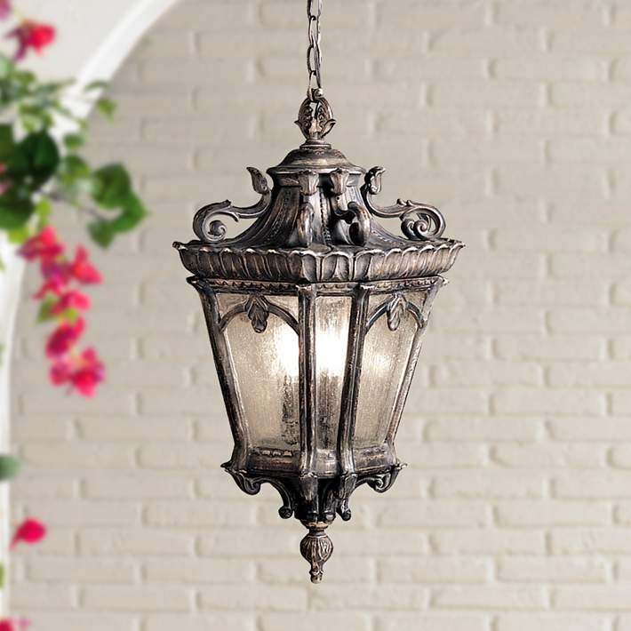 an old fashioned hanging light in front of a white brick wall with flowers on it