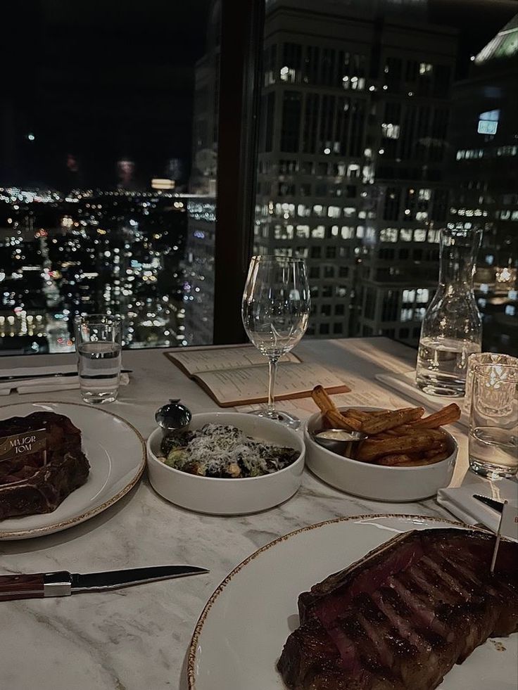 a table topped with plates and bowls filled with food next to a window at night