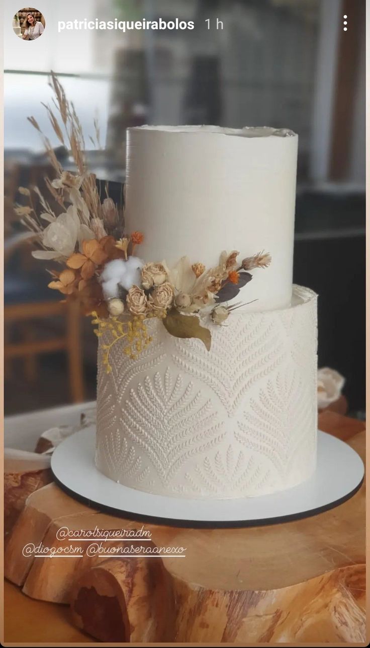 a three tiered white cake with flowers on top is sitting on a wooden table