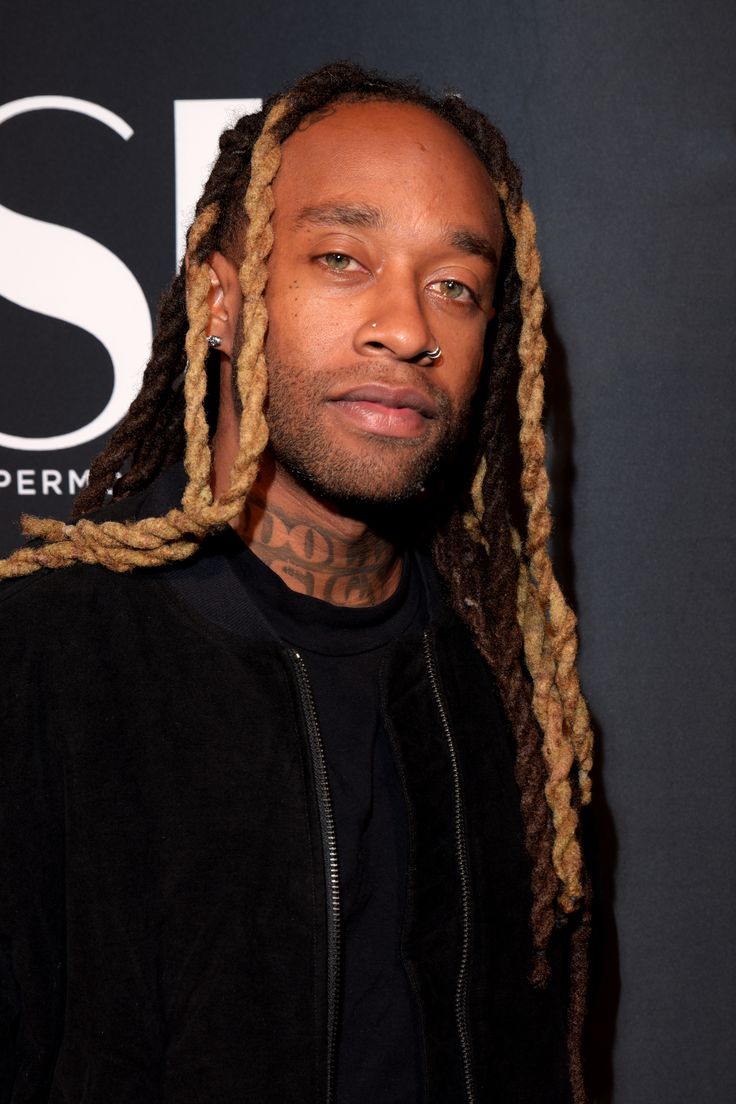 a man with dreadlocks standing in front of a wall