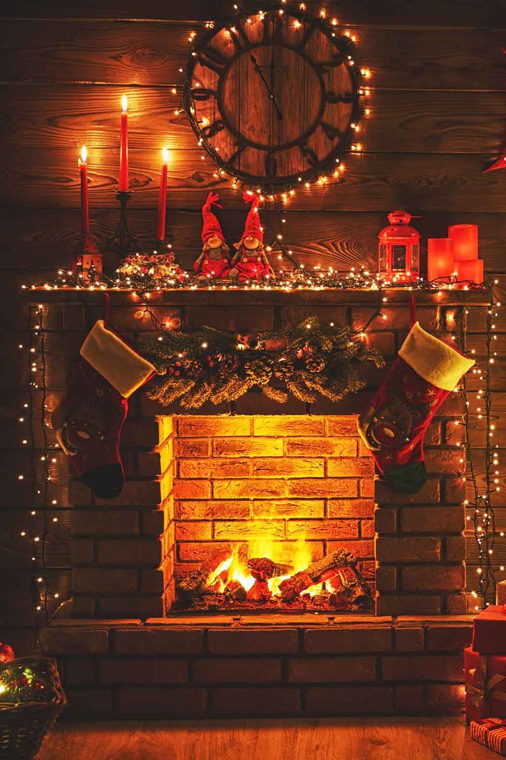 a fireplace decorated with christmas stockings, stockings and lit candles in front of a clock