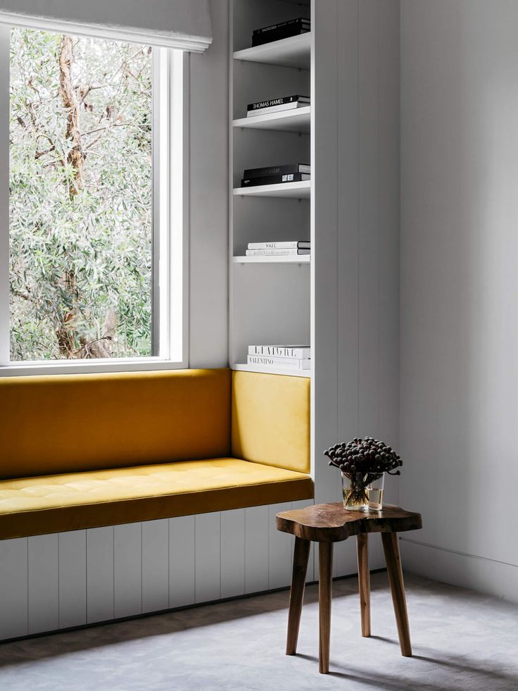 a yellow bench sitting in front of a window next to a table with a vase on it