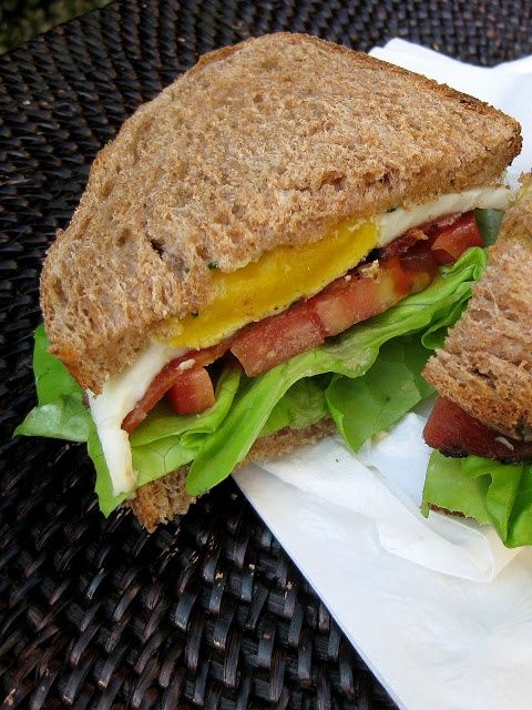 a sandwich with bacon, lettuce and cheese on it sitting on a table