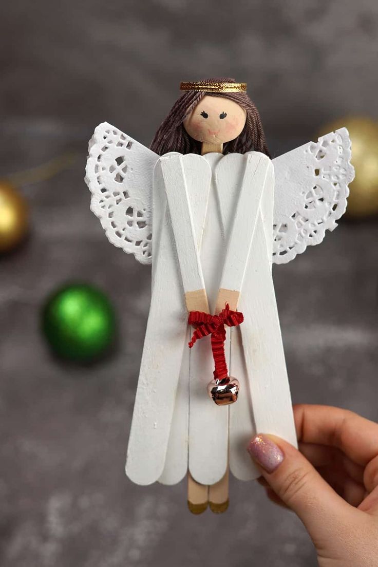 a hand holding an angel ornament made out of popsicle sticks and string