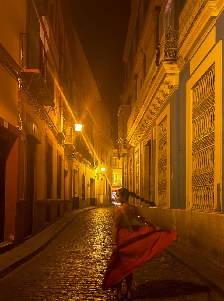 a woman in a red dress is walking down the street at night with her back to the camera